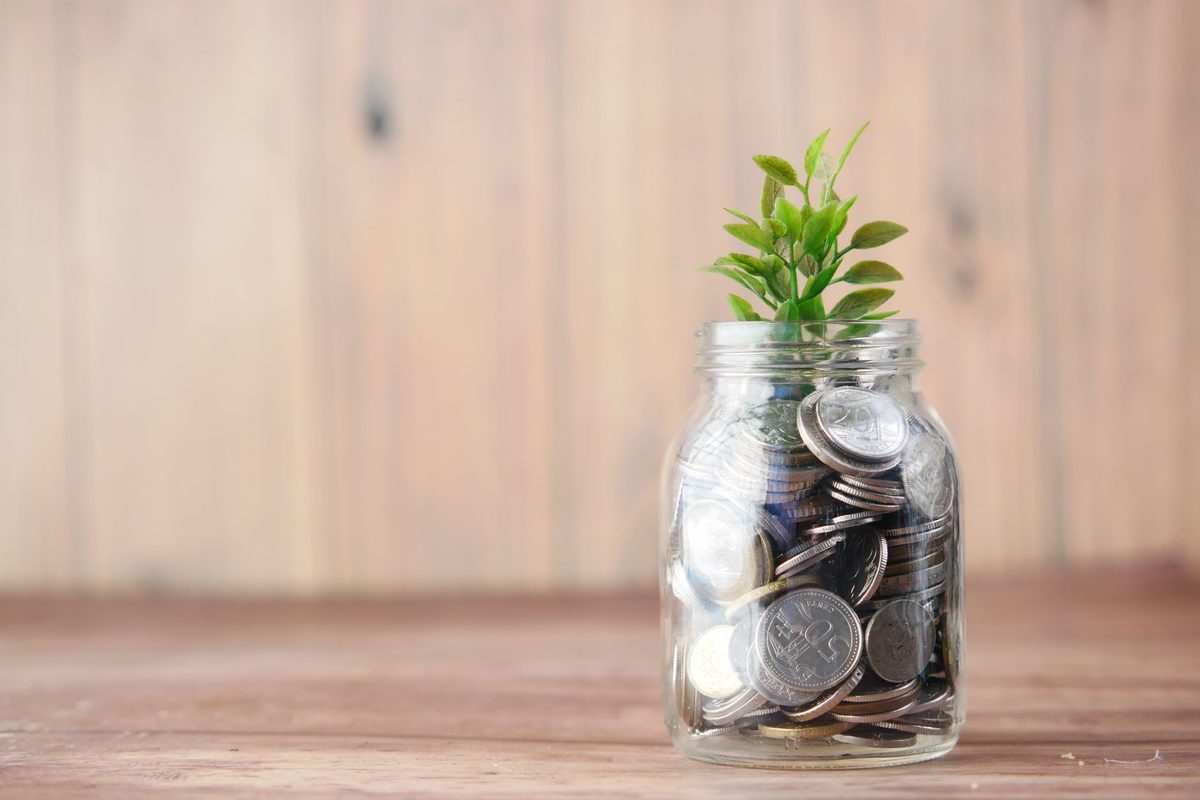A jar of coins beside a small stack of cash, representing how to start investing with only $100